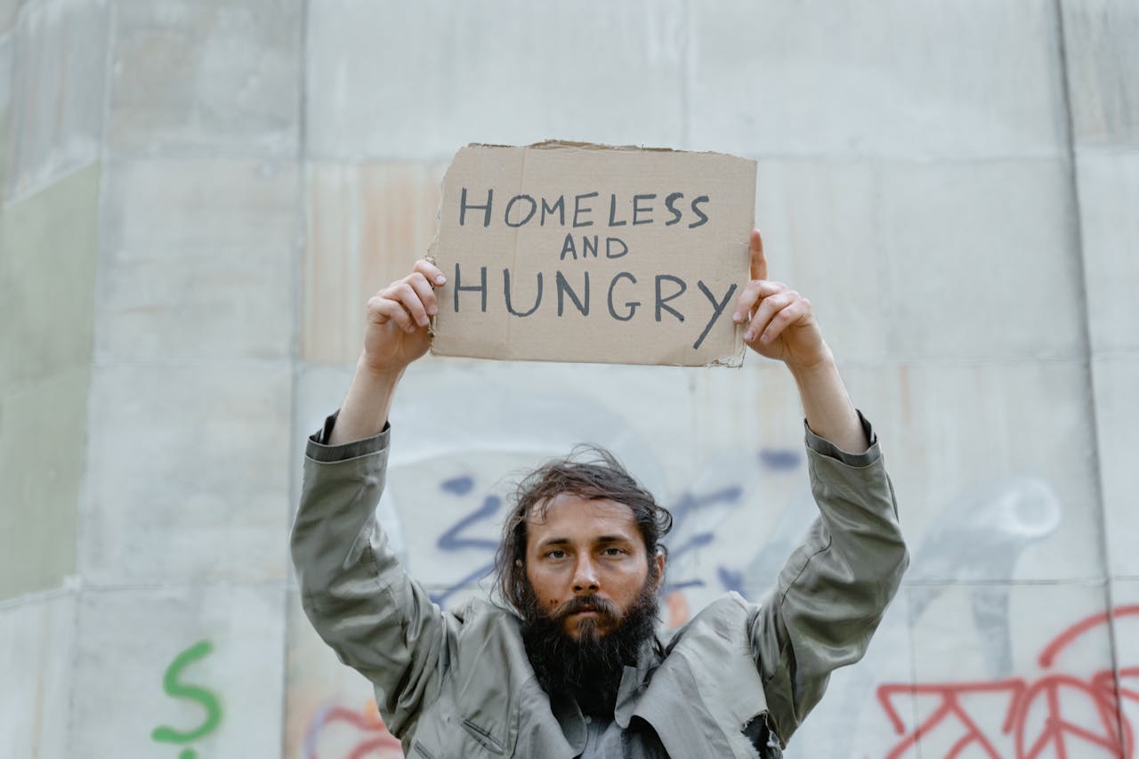 services-01 A homeless man holds a cardboard sign reading 'Homeless and Hungry.'